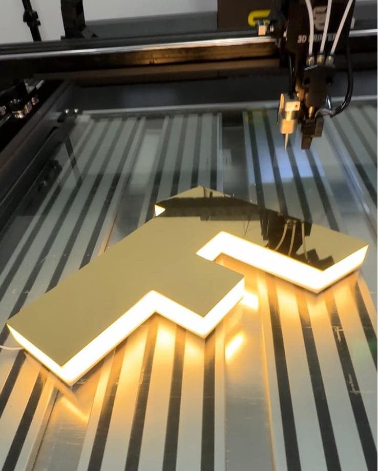A letter F with a gold face and a warm halo glow, on the printer bed