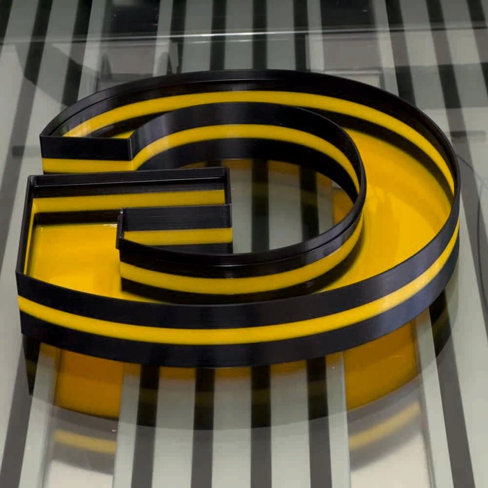 A printed letter G with a cured yellow liquid-acrylic face, mirrored as it lies face-down on the bed