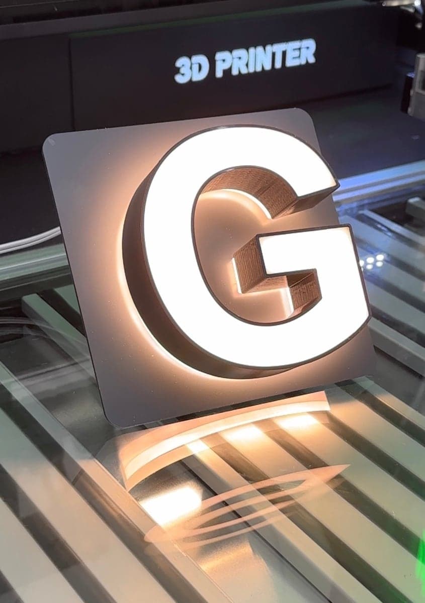 A letter G with a printed face, lit through the face and with a halo behind it, standing on the printer bed