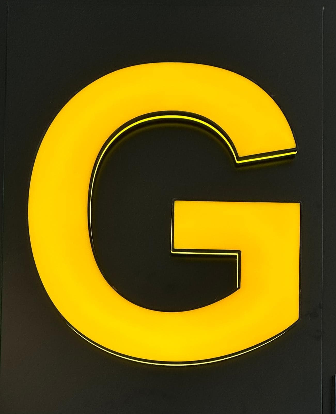 A yellow letter G with a glossy liquid-acrylic face, lit