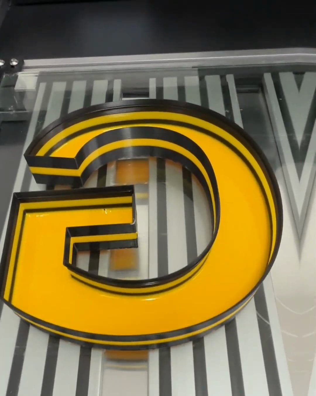A printed letter G with a yellow liquid-acrylic face, unlit on the printer bed