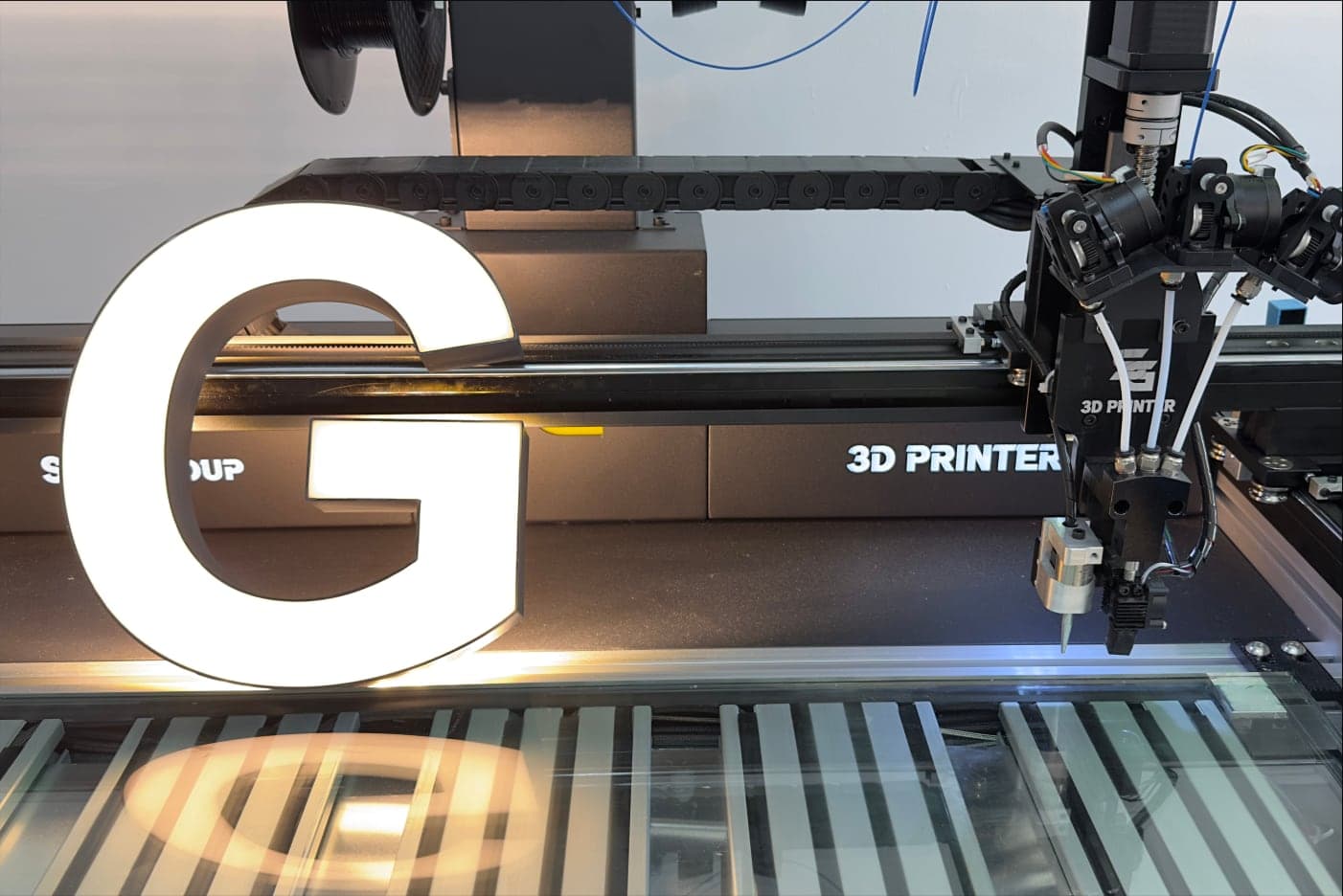 A white letter G lit on the bed of an SG letter printer, the print carriage beside it