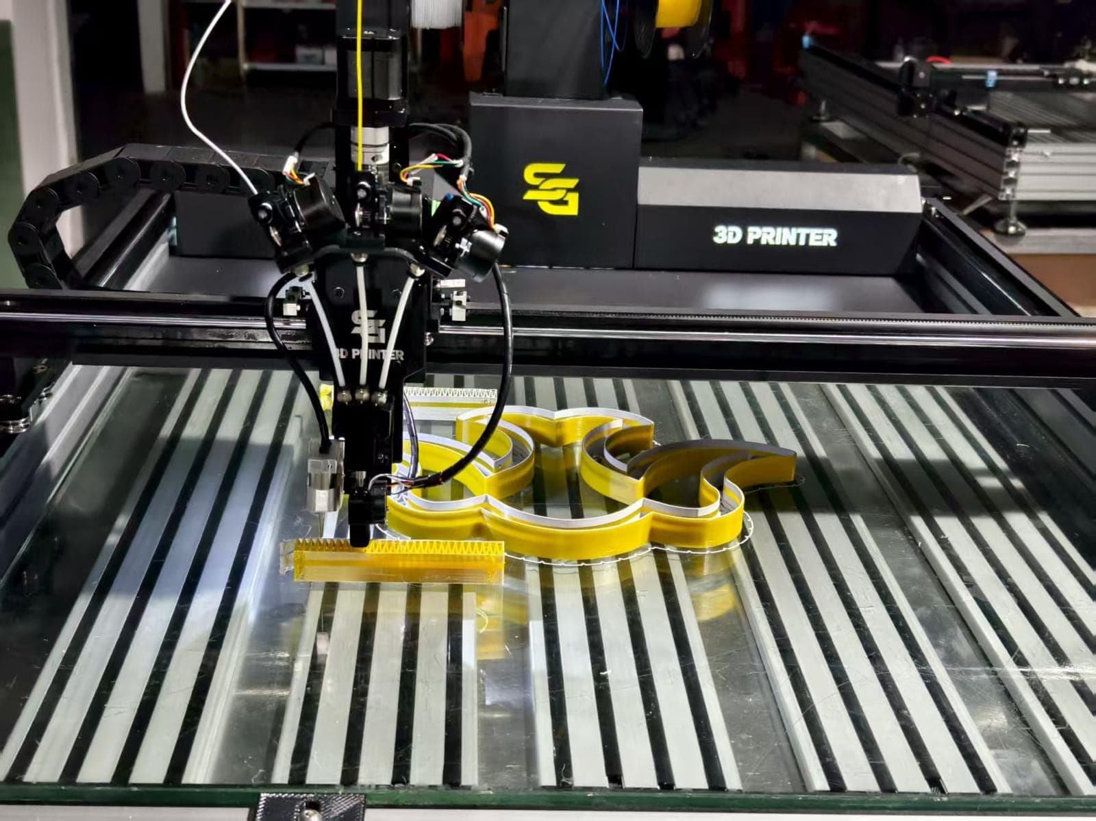 An SG letter printer's three-head carriage printing yellow letters with printed faces, mirrored on the bed